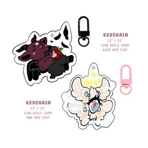 Puede incluir: Dos dijes de llavero de acr&iacute;lico de 2,5 pulgadas. Un dije presenta un demonio rosa y negro sosteniendo una manzana. El otro dije presenta un &aacute;ngel blanco y rosa con m&uacute;ltiples ojos. El dije del demonio tiene un cierre de gancho negro y el dije del &aacute;ngel tiene un cierre de gancho rosa.