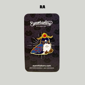 May include: Gold enamel pin featuring a cartoon bird wearing a golden crown with a sun on top. The bird has blue and red feathers and is wearing sunglasses. The pin is on a black background with a white cat pattern and the text "eyewhiskers studio" and "eyewhiskers.com".