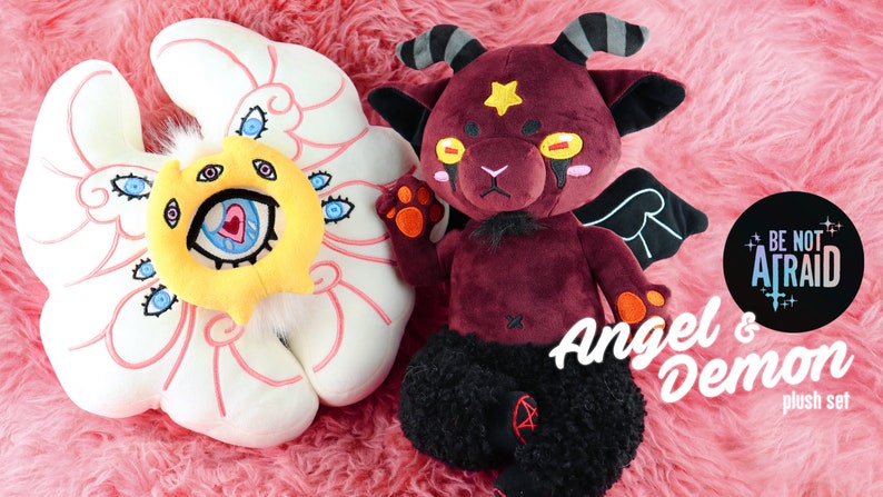 Puede incluir: Un conjunto de peluche de &aacute;ngel y demonio. El &aacute;ngel es una nube de peluche blanca con una cara amarilla y m&uacute;ltiples ojos. El demonio es un peluche burdeos con cuernos, alas y piernas negras. El texto "Be Not Afraid" y "Angel & Demon plush set" es visible en la imagen.
