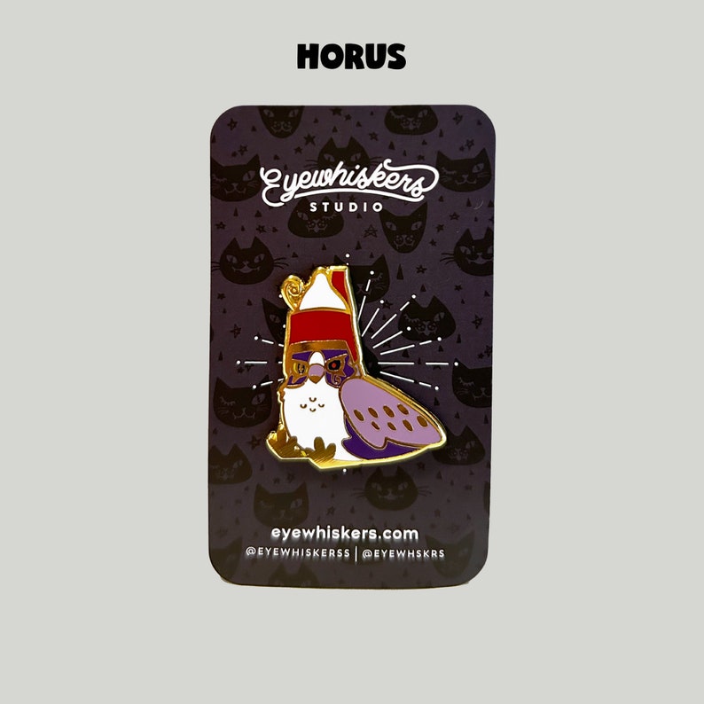May include: Gold enamel pin featuring a cartoon owl wearing a red Santa hat and sunglasses. The owl is purple and white with a gold outline. The pin is on a black card with the text "Eyewhiskers Studio" and "eyewhiskers.com".