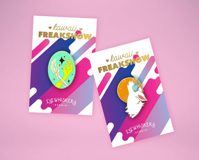 May include: Two enamel pins with a colorful background. The first pin features a green and yellow skeleton hand holding a star. The second pin features a white wolf howling at the moon. Both pins have the text "kawaii FREAKSHOW" and "EYE WHISKERS STUDIO."