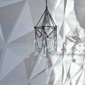 May include: A black metal chandelier with crystal prisms hanging from it. The chandelier is suspended from the ceiling and is surrounded by a white background.