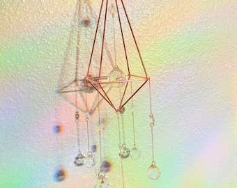 May include: A geometric copper-toned metal frame with a crystal prism hanging from the center.  The frame is suspended from the ceiling and has six crystal prisms hanging from the bottom.