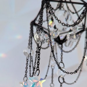 May include: A black metal geometric mobile with iridescent crystal stars and beads hanging from chains.