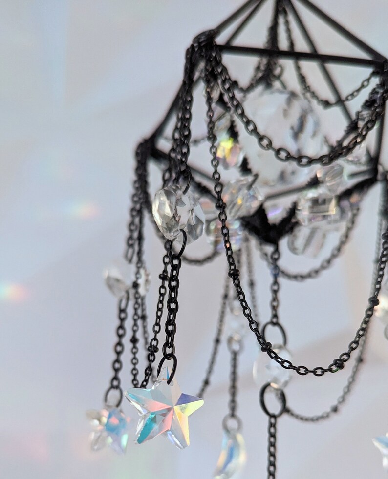 May include: A black metal geometric mobile with iridescent crystal stars and beads hanging from chains.