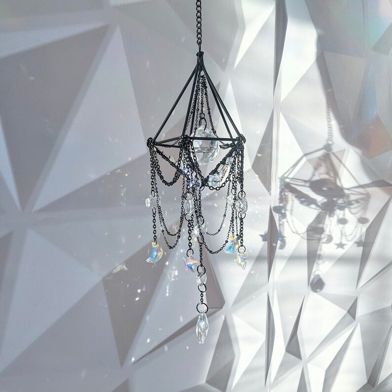 May include: A black metal chandelier with crystal prisms hanging from it. The chandelier is suspended from the ceiling and is surrounded by a white background.