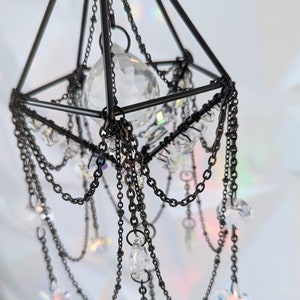 May include: A black metal geometric chandelier with crystal prisms and star-shaped accents hanging from chains.