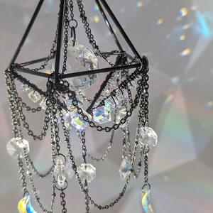 May include: A black metal geometric chandelier with crystal prisms and a large crystal orb hanging from the center. The chandelier is decorated with chains and has a modern design.