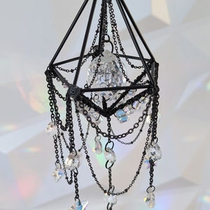 May include: A black metal geometric chandelier with crystal drops and a large crystal prism in the center.
