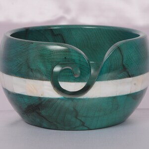 May include: A teal green wooden yarn bowl with a white mother of pearl inlay. The bowl has a carved spiral for holding yarn.