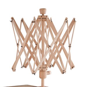 May include: A wooden yarn swift with a clamp for attaching to a table. The swift is made of natural wood and has a simple design. The clamp is labeled "Twist O' Knit".