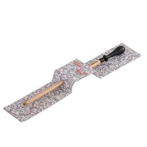 May include: A wooden knitting needle with a black plastic tip, packaged in a gray and white patterned paper wrapper. The wrapper has the text "Stitch & Story" printed on it.