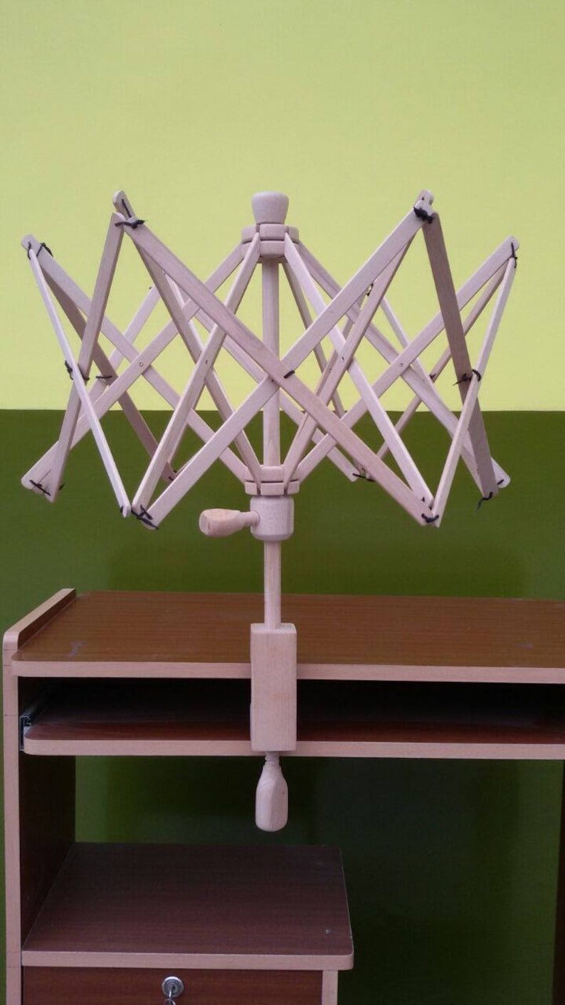 May include: A wooden yarn swift with a crank handle, mounted on a wooden table with a drawer. The swift is in a starburst shape with multiple arms.