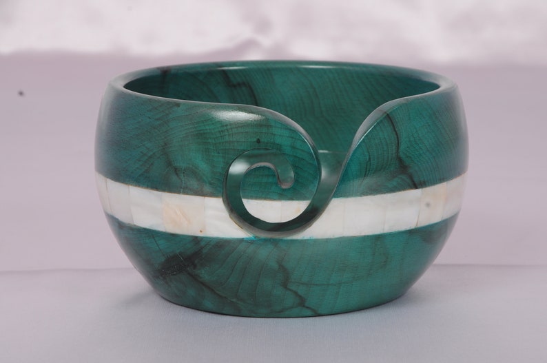 May include: A teal green wooden yarn bowl with a white mother of pearl inlay. The bowl has a carved spiral for holding yarn.