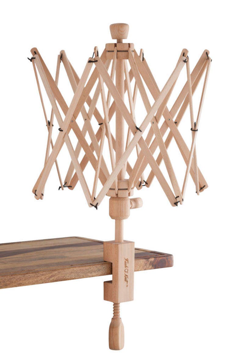 May include: A wooden yarn swift with a clamp for attaching to a table. The swift is made of natural wood and has a simple design. The clamp is labeled "Twist O' Knit".