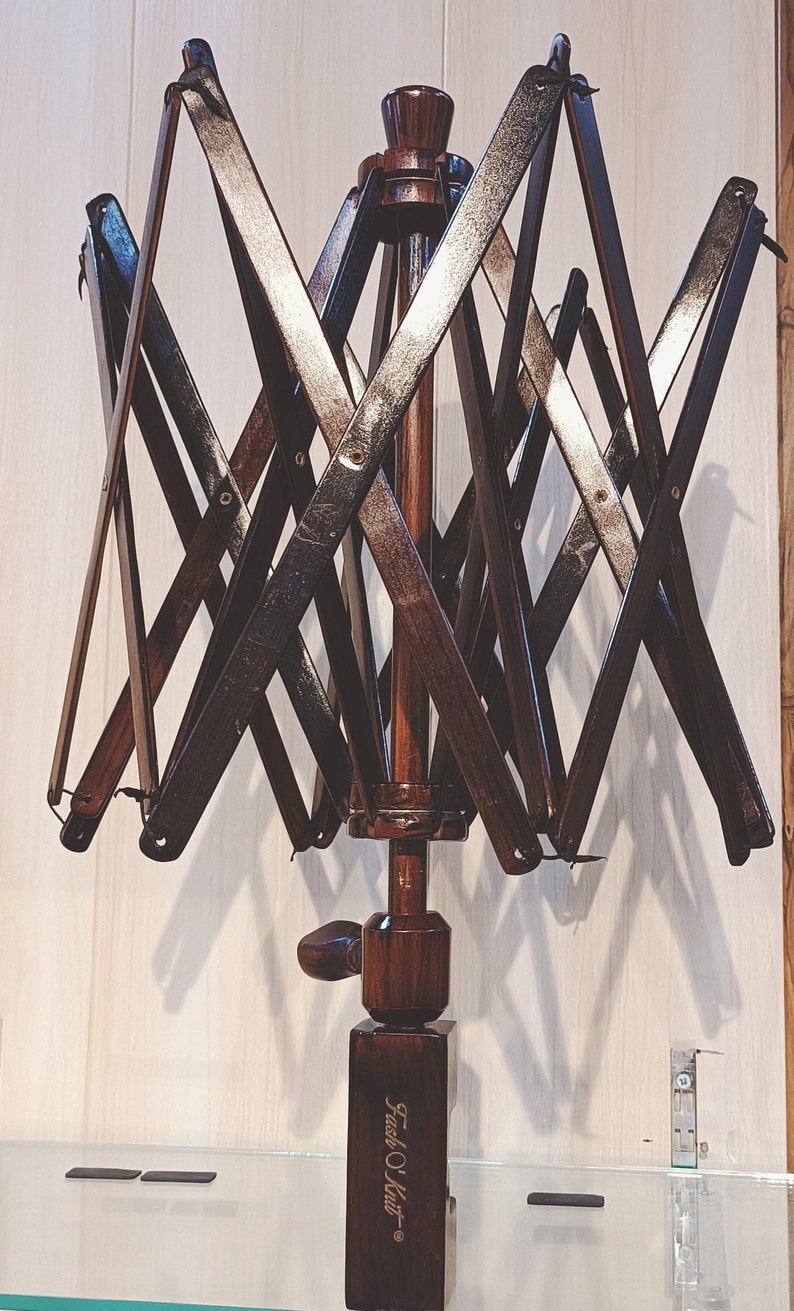 May include: A dark brown wooden yarn swift with a folding design. The swift has a crank handle and a base with the text "Furls O' Knit" engraved on it.