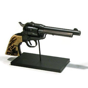 May include: Two black pistols on display stands. The pistol on the left has a brown and white handle. The pistol on the right has a black handle.