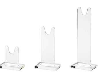 Puede incluir: Tres expositores transparentes de acrílico de diferentes alturas. Cada soporte tiene una base rectangular y una parte superior en forma de U, diseñada para sostener objetos en posición vertical. El diseño transparente permite una visión clara de los objetos expuestos.