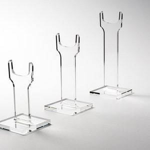 Puede incluir: Tres soportes de exhibición de acrílico transparente de diferentes tamaños para exhibir espadas u otros objetos de colección. Los soportes tienen una parte superior en forma de U y una base cuadrada.