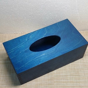 May include: A blue wooden tissue box with a rectangular shape and a rounded opening for tissues. The box is made of wood with a natural grain pattern.