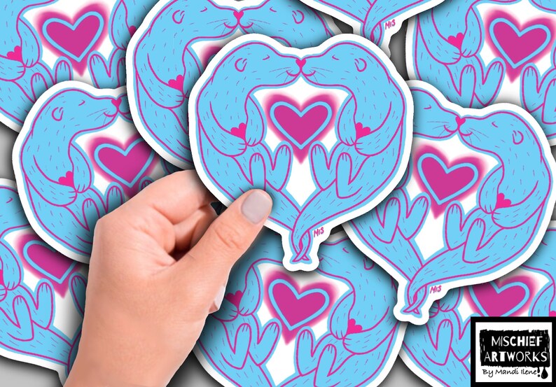 May include: A set of blue and pink otter stickers with hearts. The otters are holding hands and kissing. The stickers are on a white background.