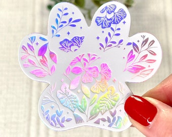 May include: A holographic paw print sticker with a floral design in rainbow colors. The sticker is on a white background.
