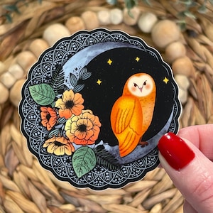 Pu&ograve; includere: Un adesivo con un gufo arancione appollaiato su una luna crescente su sfondo nero. Il gufo &egrave; circondato da fiori arancioni e foglie verdi. L'adesivo ha un bordo nero e bianco intricato.