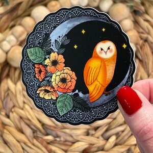 Pu&ograve; includere: Un adesivo con un gufo arancione appollaiato su una luna crescente su sfondo nero. Il gufo ha occhi gialli e una faccia bianca. La luna &egrave; circondata da un motivo floreale bianco e nero.