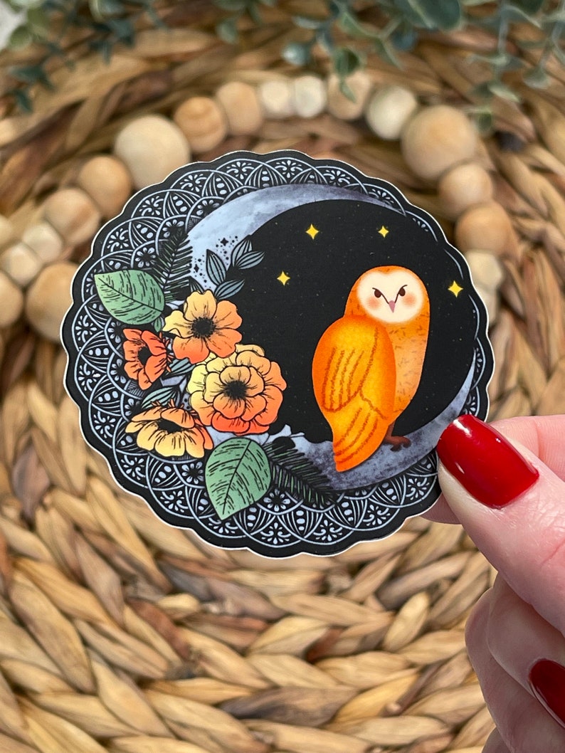 Pu&ograve; includere: Un adesivo con un'illustrazione stilizzata di un gufo arancione appollaiato su una luna crescente con stelle. Il gufo &egrave; circondato da fiori stilizzati in tonalit&agrave; di arancione, giallo e rosso. Lo sfondo &egrave; nero con un bordo decorativo.