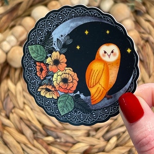 Pu&ograve; includere: Un adesivo con un'illustrazione stilizzata di un gufo arancione appollaiato su una luna crescente con un design floreale. Il gufo ha grandi occhi rotondi e un motivo di piume dettagliato. La luna &egrave; circondata da un design simile a un mandala in bianco e nero.