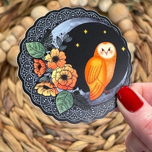 Pu&ograve; includere: Un adesivo con un gufo arancione appollaiato su una luna crescente su sfondo nero. Il gufo ha occhi gialli e un viso bianco. La luna &egrave; circondata da fiori arancioni e gialli e foglie verdi. L'adesivo ha un bordo intricato in bianco e nero.