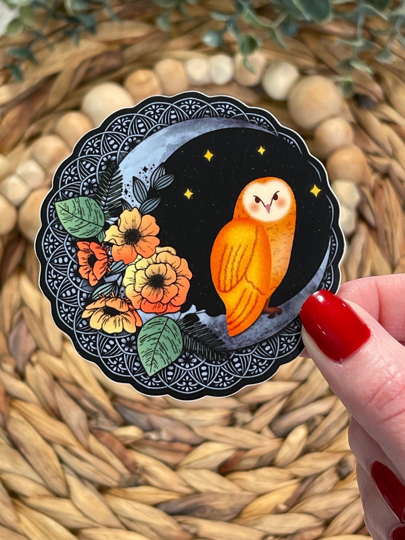 Pu&ograve; includere: Un adesivo con un gufo arancione appollaiato su una luna crescente su sfondo nero. Il gufo &egrave; circondato da fiori arancioni e foglie verdi. L'adesivo ha un bordo nero e bianco intricato.