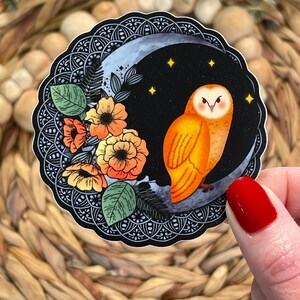 Pu&ograve; includere: Un adesivo con un'illustrazione stilizzata di un gufo arancione appollaiato su una luna crescente su sfondo nero. Il gufo ha grandi occhi gialli e un design dettagliato. La luna &egrave; circondata da un motivo mandala bianco e nero e da alcune piccole stelle gialle. Ci sono anche fiori arancioni e gialli sul lato sinistro dell'adesivo.