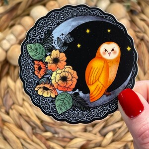 Pu&ograve; includere: Un adesivo con un gufo arancione appollaiato su una luna crescente con un design floreale. Il gufo ha occhi gialli e un becco nero. La luna &egrave; circondata da un design mandala in bianco e nero.