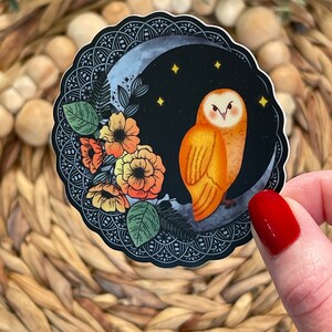 Pu&ograve; includere: Un adesivo rotondo con sfondo nero che presenta un gufo arancione appollaiato su una luna crescente con stelle. Il gufo &egrave; circondato da fiori arancioni, gialli e rossi con foglie verdi. L'adesivo ha un bordo intricato in bianco e nero.