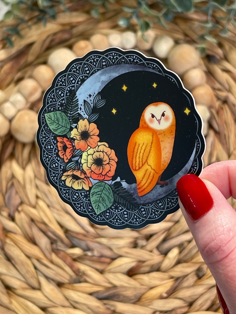 Pu&ograve; includere: Un adesivo rotondo con sfondo nero che presenta un gufo arancione appollaiato su una luna crescente con stelle. Il gufo &egrave; circondato da fiori arancioni, gialli e rossi con foglie verdi. L'adesivo ha un bordo intricato in bianco e nero.