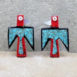 Puede incluir: Par de pendientes artesanales con forma de pájaro. Los pendientes presentan un cuerpo rojo, contorno negro y alas con incrustaciones de turquesa. La cabeza del pájaro es roja con un ojo blanco y un pico plateado. Los pendientes están sobre un fondo neutro.