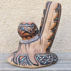 May include: A hand-painted ceramic pipe in the shape of a tree stump with a bowl on top. The pipe is decorated with brown, black, and turquoise geometric patterns.
