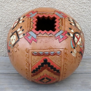 May include: A round, terracotta-colored ceramic pot with a geometric design in red, black, white, and blue. The pot has a square opening at the top.