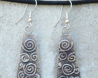 May include: A pair of silver-coloured earrings with a textured, trapezoid shape. Each earring features embossed spiral designs. The earrings hang from silver-coloured fish hook ear wires.