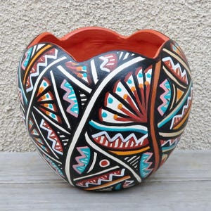 May include: A black ceramic planter with a heart shape and a geometric pattern in orange, white, red, blue, and pink.