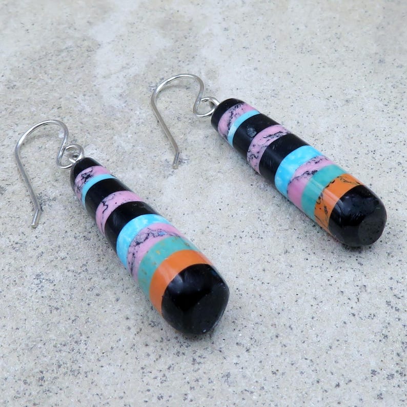 May include: A pair of dangle earrings with a black, cylindrical design. The earrings feature horizontal stripes in pink, black, blue, green, and orange. The earrings have silver-coloured hooks.