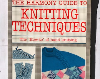 Può includere: Copertina di un libro vintage con il titolo "THE HARMONY GUIDE TO KNITTING TECHNIQUES" in rosso. La copertina presenta illustrazioni di maglieria e una foto di un maglione blu lavorato a maglia e una coperta patchwork. Il sottotitolo recita "The 'How-to' of hand knitting."