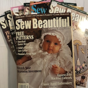 Puede incluir: Una pila de revistas de costura vintage, incluyendo "Sew Beautiful" con un bebé en la portada. Las revistas presentan artículos sobre bordado, moda femenina e infantil y reliquias clásicas. La portada de "Sew Beautiful" incluye el texto "Free Patterns".