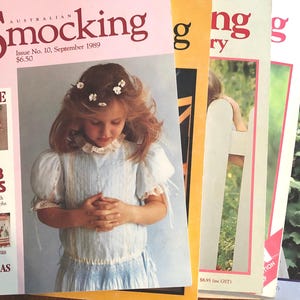 Könnte beinhalten: Ein Stapel von fünf Magazinen mit bunten Covern. Das vordere Magazin ist mit "Australian Smocking" betitelt, mit der Nummer und dem Datum der Ausgabe. Das Magazin zeigt ein junges Mädchen, das ein hellblaues Smockshirt mit weißem Kragen trägt. Das Titelbild des Magazins enthält auch eine kleine Illustration eines floralen Stickmusters.