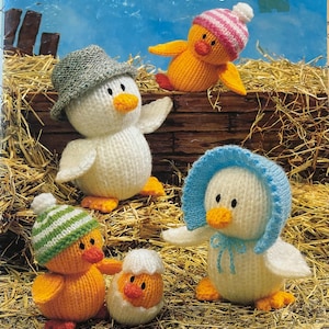 Puede incluir: Portada del libro "Jean Greenhowe's Knitted Animals" con varios patitos tejidos. Los patitos son blancos y naranjas, con sombreros de varios colores. El fondo incluye heno y tablones de madera. También se ve el texto "Irresistible soft toy designs".