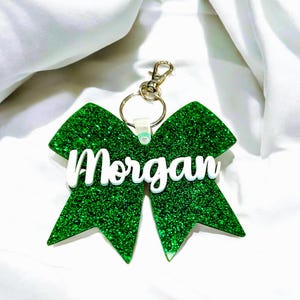 May include: Green glitter bow keychain with the name "Morgan" in white lettering.