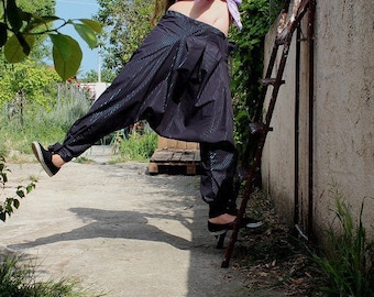 May include: A person wearing a striped black and blue pants with a light purple shirt tied at the waist. The person is standing on a concrete surface with a ladder and a wall in the background.
