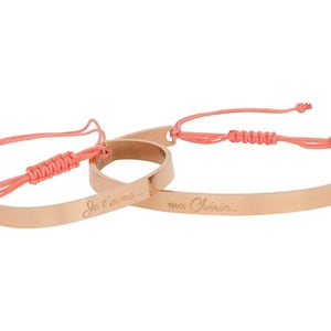 May include: Two rose gold bracelets with pink string ties. The bracelets are engraved with the phrases "Je t'aime" and "mon Cherie".
