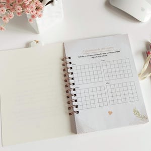 May include: A white and gold spiral bound notebook with a calendar grid on the right page. The calendar grid is labeled "Calendario de mis metas" and has a section for each month. The left page is blank.
